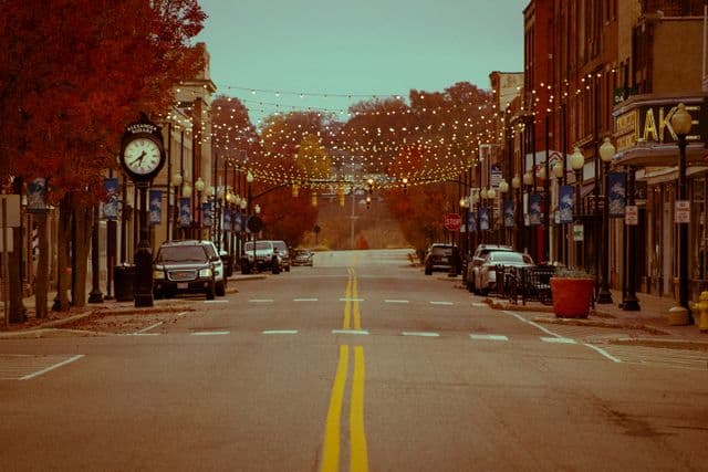 A downtown street at dusk, strung with lights over the road and storefronts