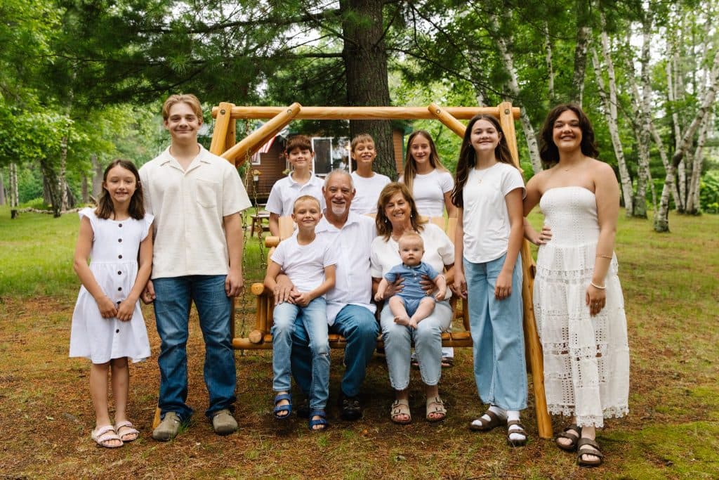Curt and his wife on a wooden porch swing surrounded by their children and grandchildren